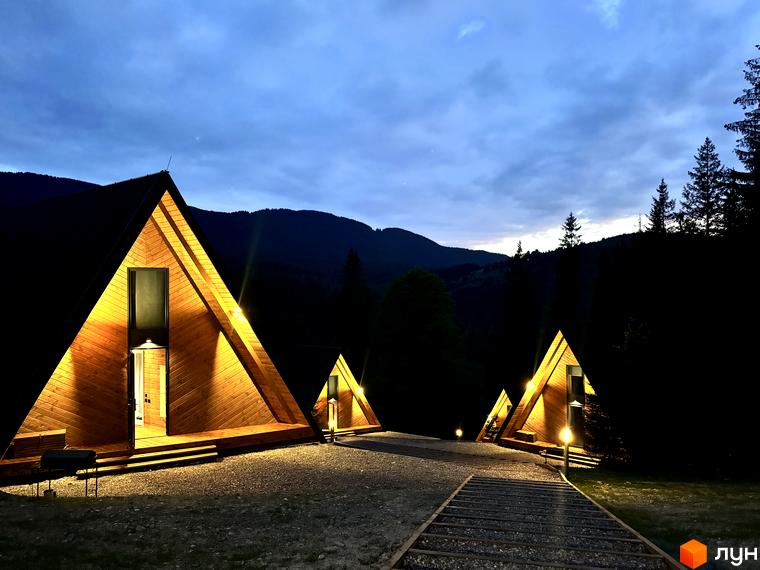 Комплекс відпочинку УЛІС. Трикутні дерев'яні будиночки з підсвіткою в темряві на фоні гір та лісу.