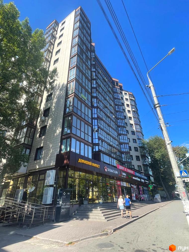 Новобудова ЖК Pirogovsky з панорамними вікнами та комерційними приміщеннями на першому поверсі. Поруч розташовані дерева та міська вулиця з пішохідною зоною.