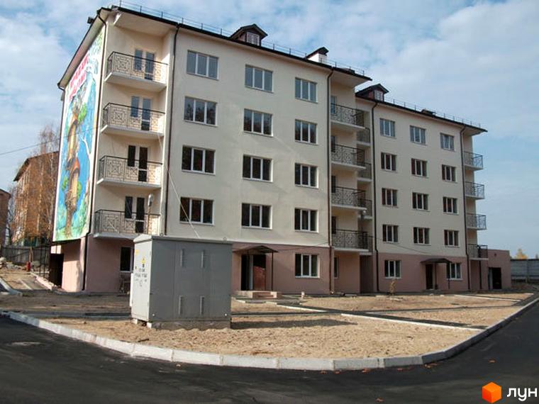 Житловий комплекс Милдом. Зовнішній вигляд чотириповерхового будинку з балконами та вікнами. Прибудинкова територія з піском та дорогою.
