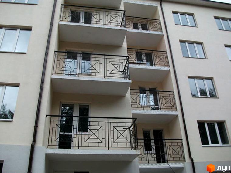 Зовнішній вигляд житлового комплексу Милдом з балконами та вікнами. Будинок з сірим фасадом та чорними кованими решітками на балконах.