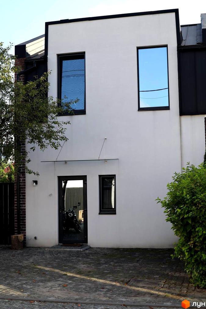 Фасад таунхаусу в Житловому районі Lisostepoville з великими вікнами та вхідними дверима. Подвір’я вимощене бруківкою.