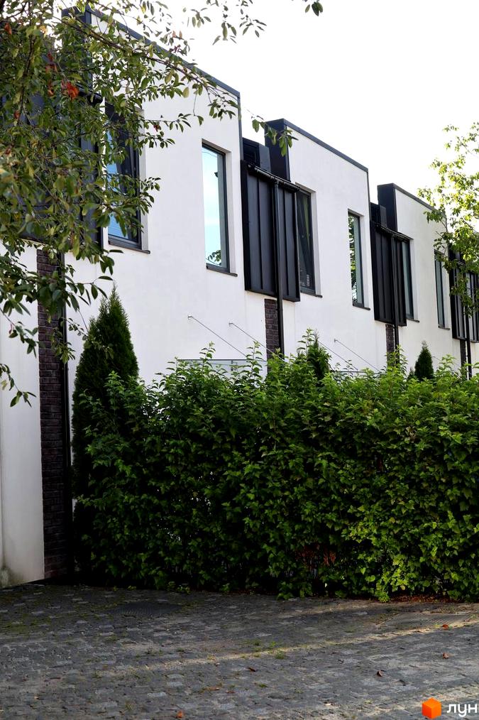 Таунхауси Lisostepoville: сучасні білі фасади з чорними елементами, великі вікна та зелений доглянутий двір з бруківкою.