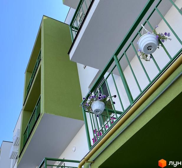 Житловий комплекс Art Misto з яскравим зеленим фасадом та балконами, прикрашеними квітами у підвісних кашпо.