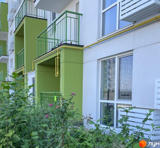 Зовнішній вигляд новобудови ЖК Art Misto з зеленими балконами та білими фасадами. Прибудинкова територія з зеленню та квітами.