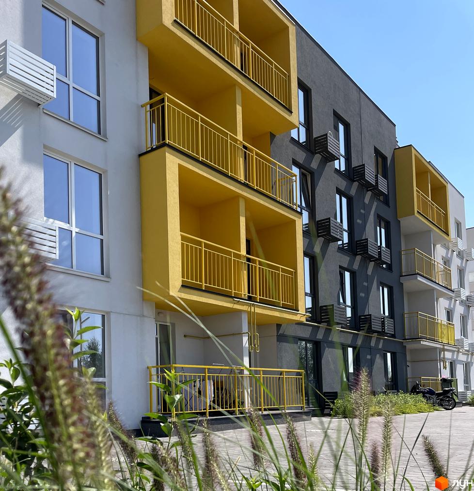 Житловий комплекс Art Misto: біла та сіра будівлі з жовтими балконами та геометричним фасадом. Перед будинком вимощена територія з рослинністю.