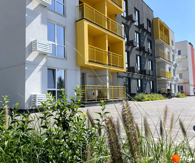 Зовнішній вигляд новобудови ЖК Art Misto з жовтими балконами та сірими фасадами. Прибудинкова територія з зеленими насадженнями та бруківкою.