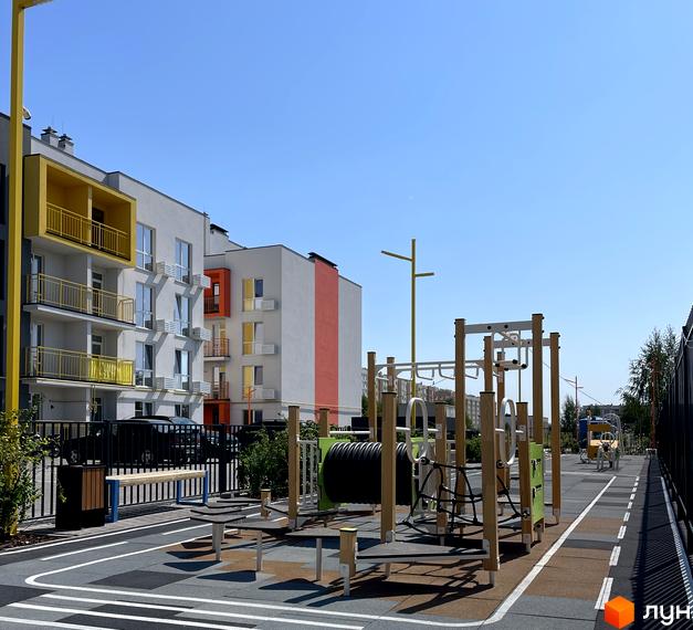 Житловий комплекс Art Misto: білі фасади з жовтими та помаранчевими акцентами, балкони та дитячий майданчик з дерев'яними елементами.