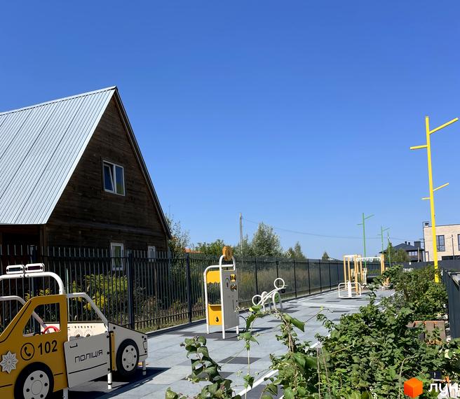 Будинок ЖК Art Misto з дерев'яним фасадом та металевим дахом. Поруч дитячий майданчик з ігровою зоною у вигляді поліцейської машини та спортивними тренажерами.