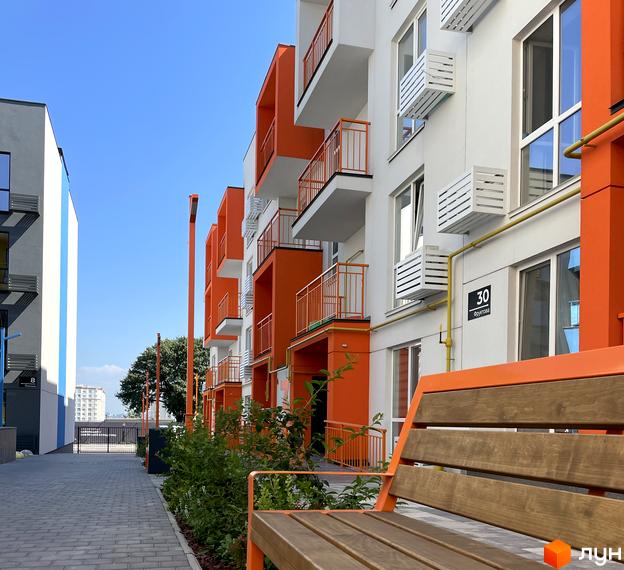 Житловий комплекс Art Misto з яскравими помаранчевими фасадами та балконами. Перед будинком розташована вимощена алея та зелені насадження.