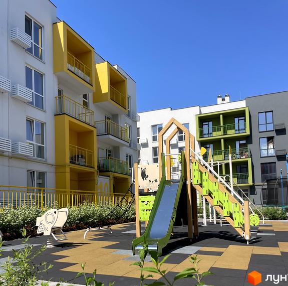 Житловий комплекс Art Misto з яскравими жовтими та зеленими фасадами та дитячим майданчиком з гіркою та гойдалкою.