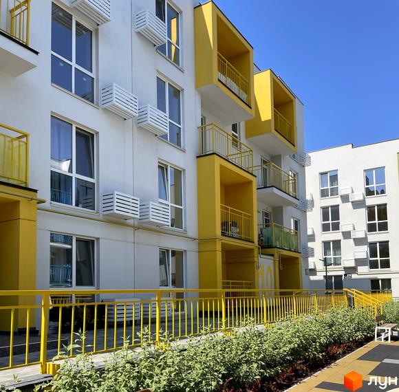 Зовнішній вигляд новобудови ЖК Art Misto з жовтими елементами та балконами. Прибудинкова територія з зеленими насадженнями та огорожею.