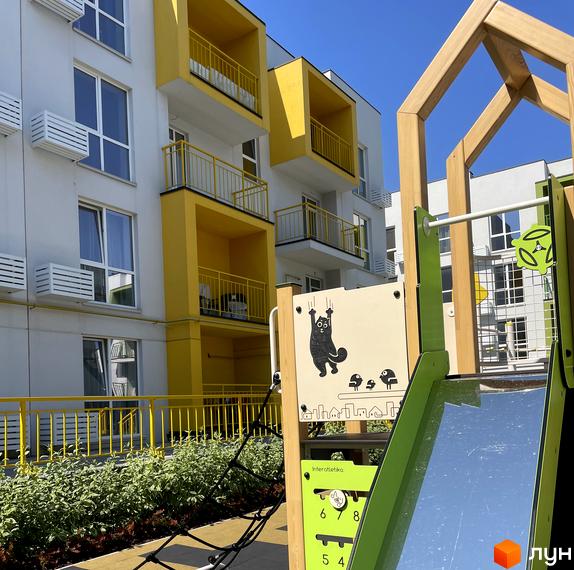 Будівельний проєкт Art Misto з яскравими жовтими елементами та дитячим майданчиком. Навколо новобудови зелена зона та паркан.