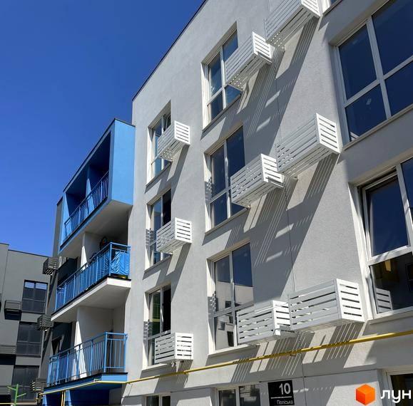 Фасад житлового комплексу Art Misto з білими кондиціонерними блоками та синіми балконами. Навколо будинку видно елементи прибудинкової території та сусідні будівлі.