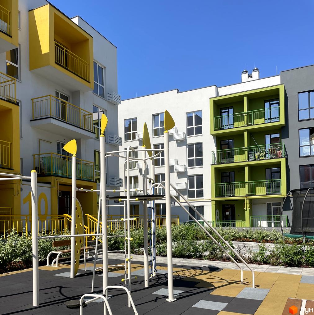 Житловий комплекс Art Misto з яскравими фасадами жовтого та зеленого кольорів. На прибудинковій території розташований сучасний дитячий майданчик з різнокольоровим покриттям.