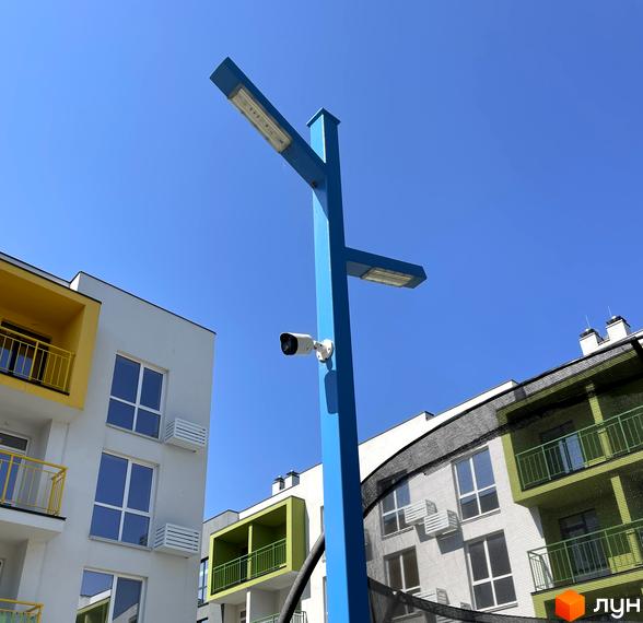 Новобудова ЖК Art Misto з яскравими фасадами та балконами на тлі блакитного неба. Біля будинку встановлено стовп з ліхтарями та камерою спостереження.