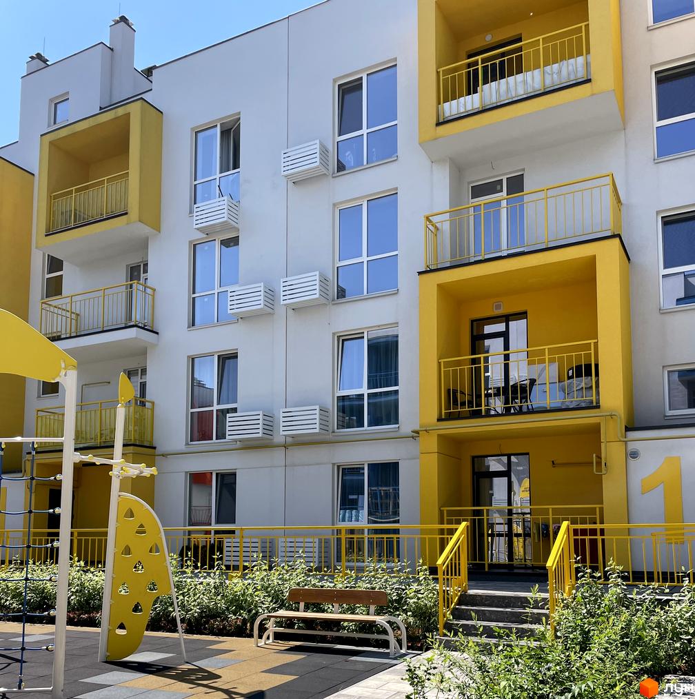 Зовнішній вигляд новобудови ЖК Art Misto з жовтими елементами та дитячим майданчиком. Фасад будинку з балконами та кондиціонерами.