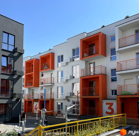 Житловий комплекс Art Misto з яскравими помаранчевими балконами та сірими фасадами. На прибудинковій території розташовані спортивні тренажери під відкритим небом.