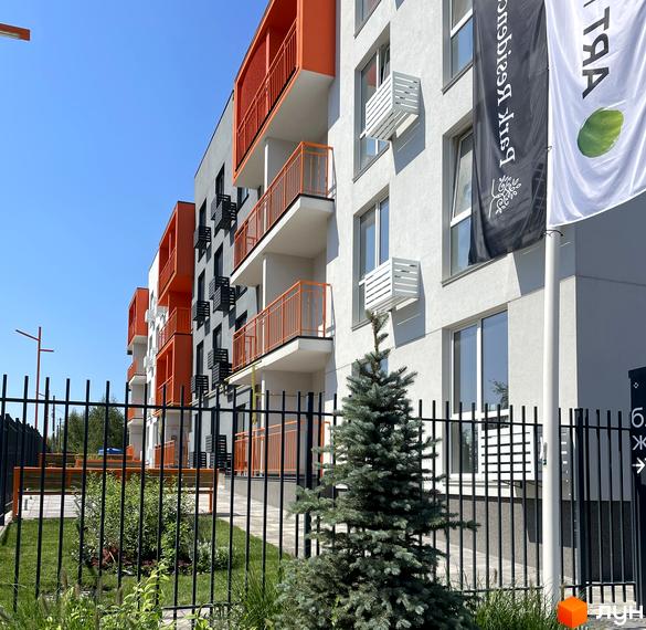 Житловий комплекс Art Misto з яскравими помаранчевими балконами на тлі блакитного неба. Територія перед будинком огороджена парканом, за яким видно зелень та дерева.