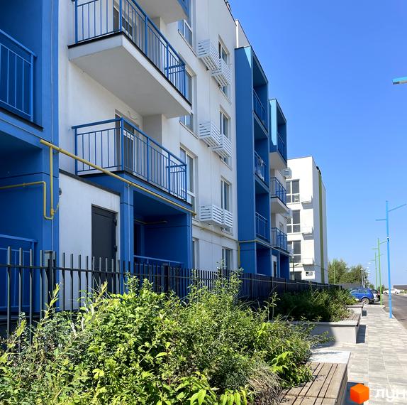 Житловий комплекс Art Misto з біло-синіми фасадами та балконами. На прибудинковій території зелені насадження та лавки.