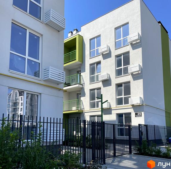 Новобудова ЖК Art Misto з білими фасадами та зеленими елементами. Огороджена територія з кущами та деревами.