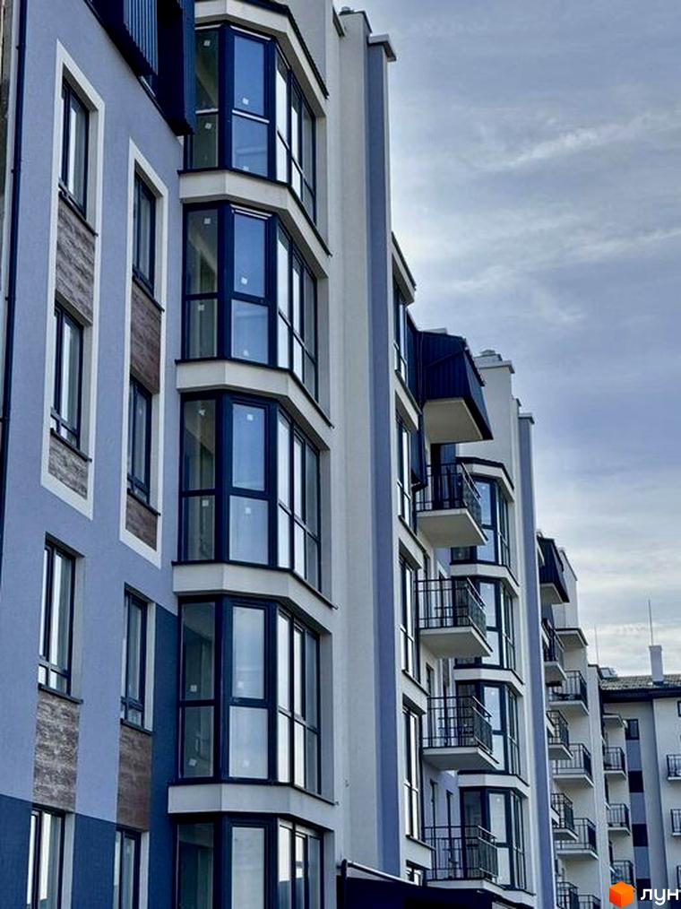 Зовнішній вигляд новобудови ЖК 9 Район з балконами та великими вікнами. Фасад будинку виконаний у світлих тонах з елементами дерев'яної обшивки.