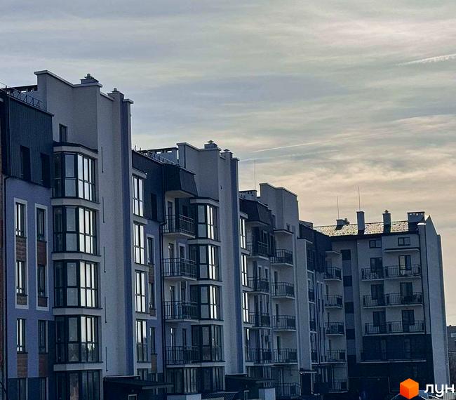 Фасад житлового комплексу 9 Район з багатоповерховими будинками та еркерними вікнами під сірим небом.