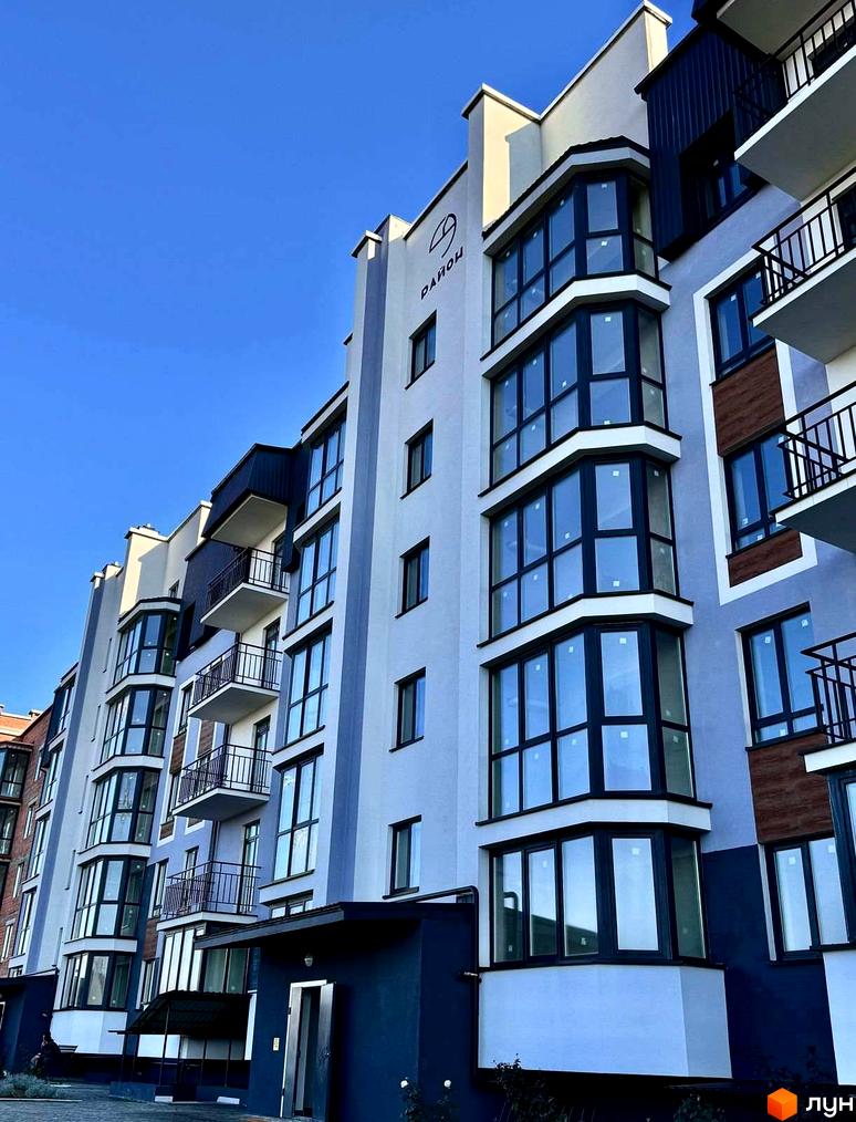 Зовнішній вигляд новобудови ЖК 9 Район з великими вікнами та балконами. Фасад будинку світло-сірого кольору з темними елементами.