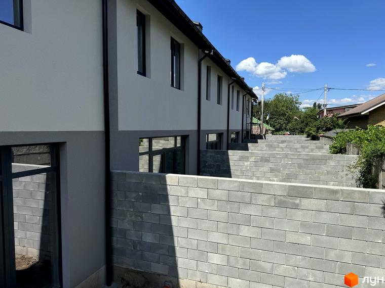 Зовнішній вигляд таунхаусів Дивногорський з сірими стінами та чорними вікнами. На передньому плані видно цегляний паркан.