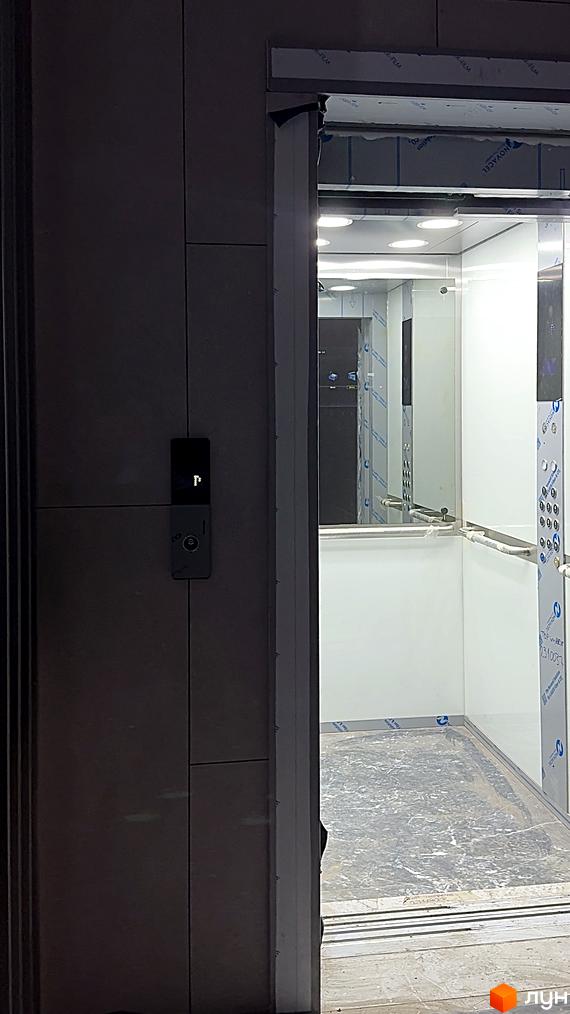 Зовнішній вигляд новобудови ЖК AcademHoff з підсвіченим входом та елементами фасаду. Всередині видно оздоблення ліфта.