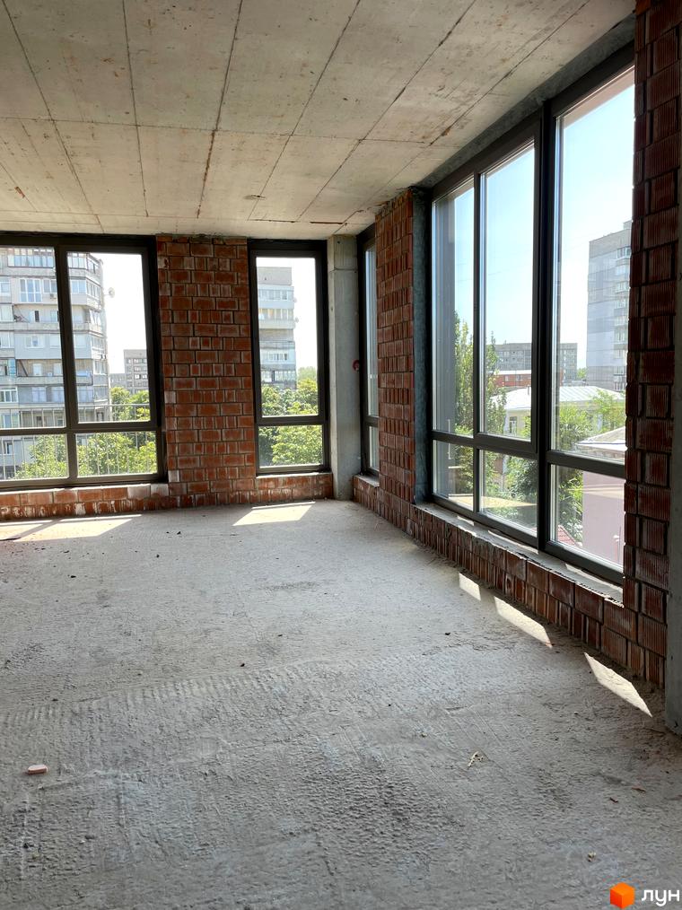 Простора кімната з панорамними вікнами та цегляними стінами в новобудові ЖК AcademHoff. Будівельний проєкт з великими вікнами та видом на міські будівлі.