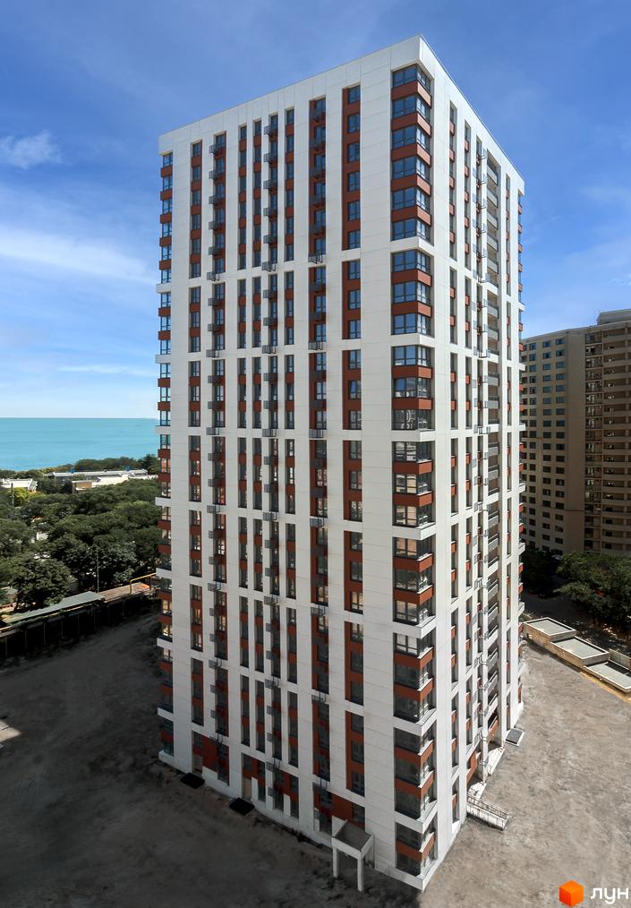 Зовнішній вигляд новобудови ЖК Sea View з білими фасадами та коричневими елементами. Поруч зелені насадження та вид на море.