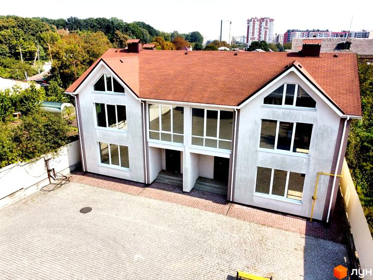 Котеджне містечко На Вишневій: двоповерховий будинок з коричневим дахом та великими вікнами, вимощена бруківкою прибудинкова територія.