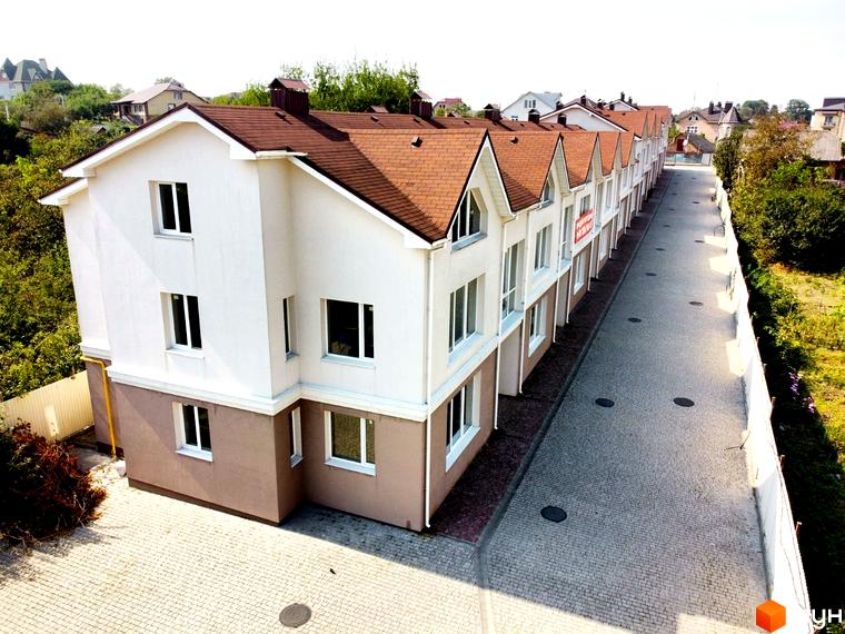 Котеджне містечко На Вишневій: фасади білих будинків з коричневими дахами та бруківка на прибудинковій території.