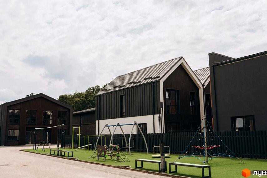 Котеджне містечко КМ Garden Village Ozerne: двоповерхові будинки з темними фасадами та металевими дахами, дитячий майданчик з гойдалками та гірками.