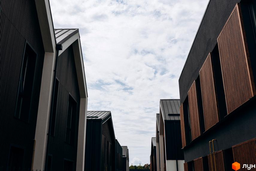 Котеджне містечко Garden Village Ozerne: фасади будинків з темним оздобленням та дерев'яними елементами на тлі хмарного неба. Сучасна архітектура новобудови.