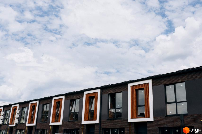 Котеджне містечко Garden Village Ozerne. Фасад будинку з коричневої цегли та темних панелей, вікна з дерев'яними вставками.