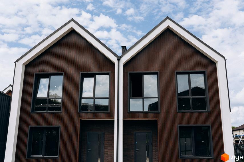 Сучасний котеджний комплекс КМ Garden Village Ozerne з коричневим фасадом та великими вікнами. Фасад будинку оздоблений вертикальними дерев'яними панелями.