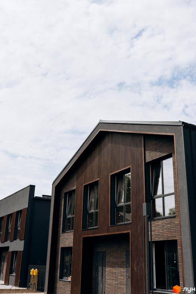 Котеджне містечко Garden Village Ozerne. Зовнішній вигляд будинків з дерев'яним фасадом та великими вікнами на фоні хмарного неба.