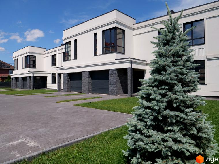 Білосніжні будинки з темними вікнами та гаражами в ЖК. На передньому плані – доглянута прибудинкова територія з бруківкою та зеленню.