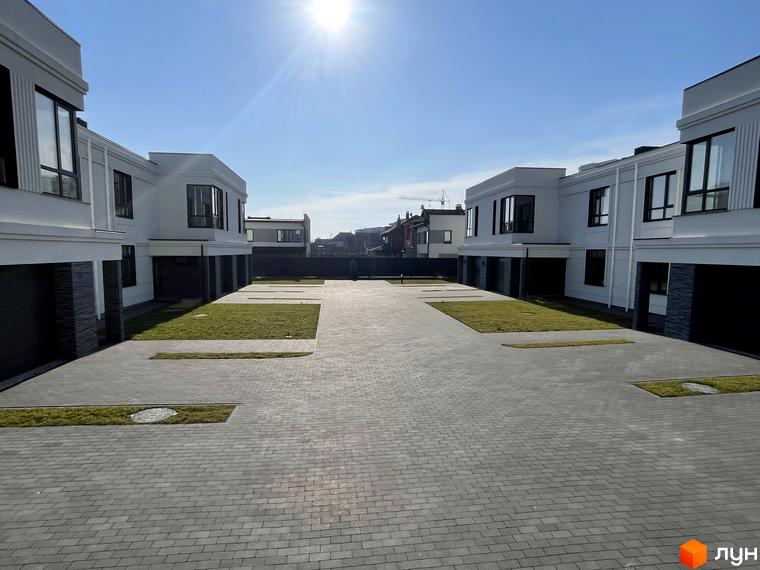 Білі будинки з темними вікнами та гаражами, викладені бруківкою доріжки та газони. ЖК на вулиці Яблунева, 4-6.