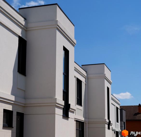 Білі будинки з великими вікнами на тлі блакитного неба. Фасад будівлі з чіткими лініями та декоративними елементами.