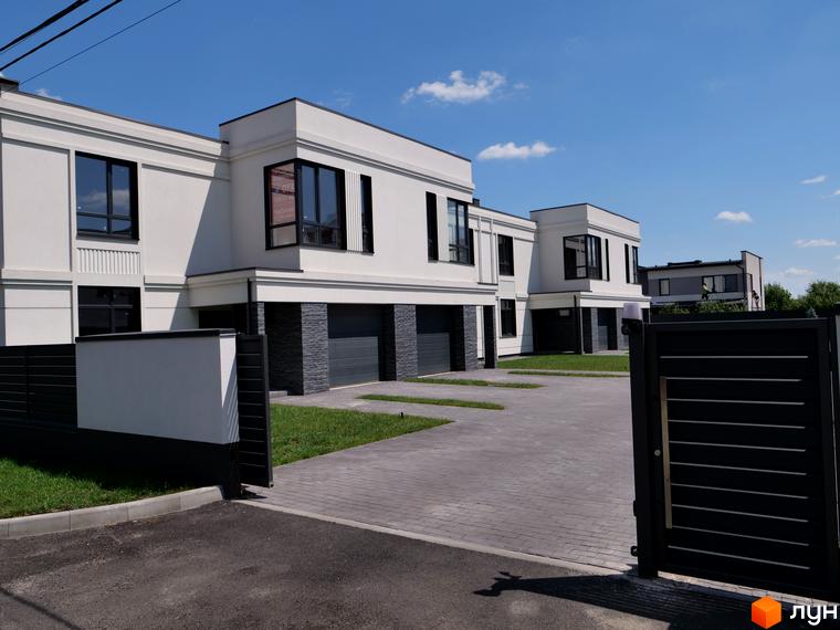 Білосніжні будинки з темними вікнами та гаражами. Простора прибудинкова територія з бруківкою та газонами, огороджена темним парканом.