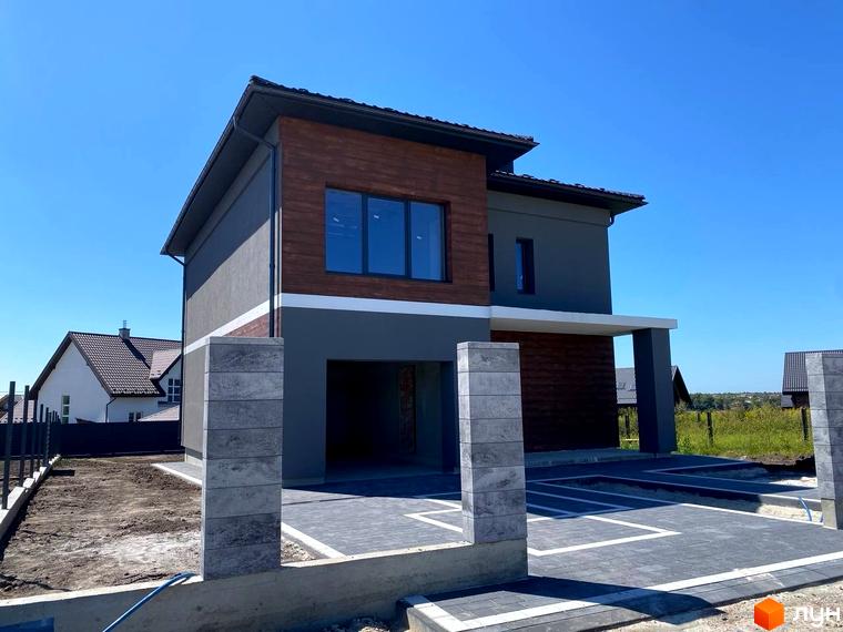 Сучасний двоповерховий будинок з дерев'яними елементами фасаду та сірим оздобленням. Прибудинкова територія з бруківкою та парканом.