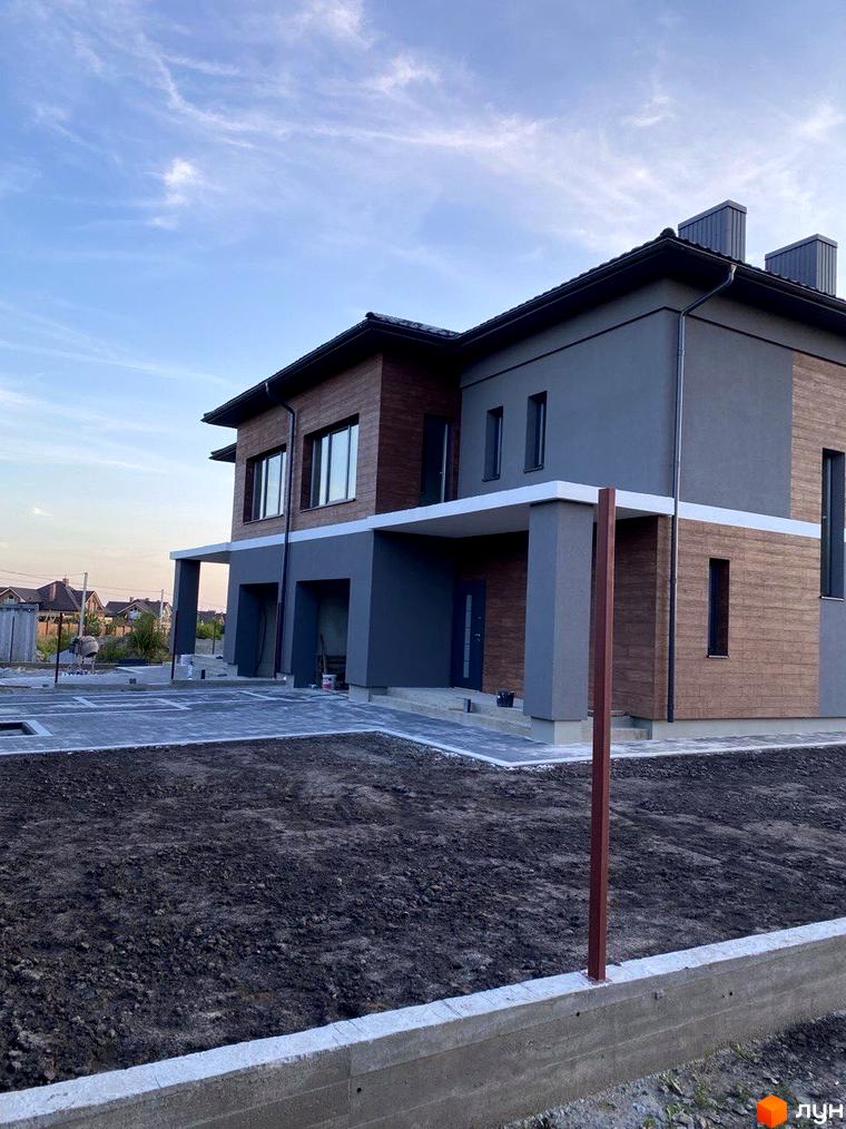 Зовнішній вигляд двоповерхового будинку з сірою та дерев'яною обробкою на вулиці Волошкова. Навколо будинку облаштована прибудинкова територія з бруківкою та зеленими насадженнями.