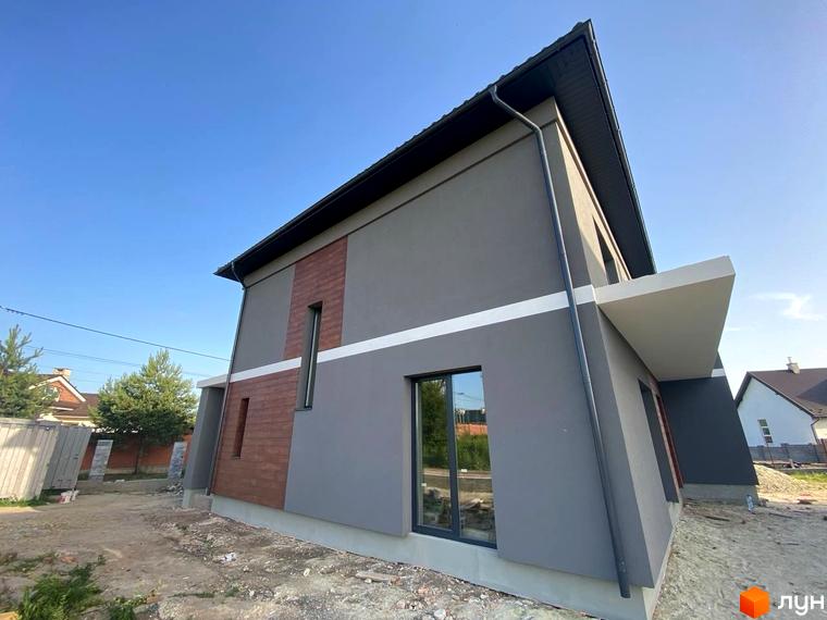 Зовнішній вигляд двоповерхового будинку з сірим фасадом та коричневими вставками на вулиці Волошкова. Навколо будинку видно будівельні роботи та зелені насадження.