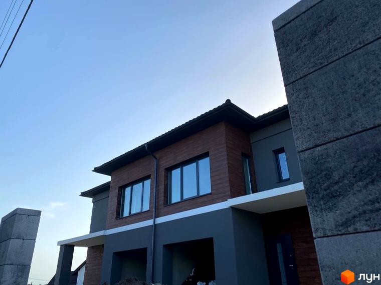 Будинок з коричневою та сірою обробкою на вулиці Волошкова. Зовнішній вигляд новобудови з великими вікнами та навісами.