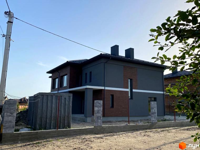 Сучасний двоповерховий будинок з темною та дерев'яною обробкою фасаду на вулиці Волошкова. Навколо будинку розташована огорожа та елементи благоустрою території.