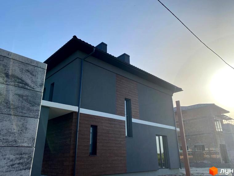 Зображення фасаду будинку на вулиці Волошковій. Новобудова з оздобленням деревом та сірими стінами.