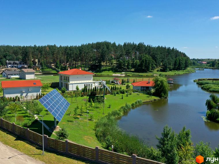 Котеджне містечко КМ Swisstown. Будинки з червоними дахами біля озера, зелена територія з сонячними панелями та лісом.