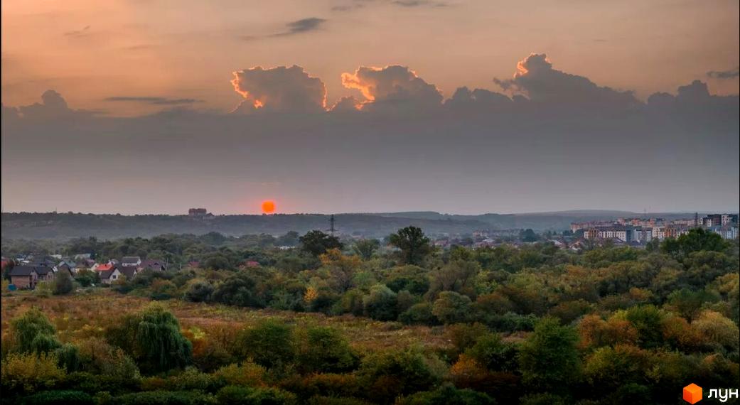 Житловий комплекс Comfort Lite з багатоповерховими будинками на тлі хмарного неба та зелених дерев. Навколо комплексу розташовані житлові будинки та густі ліси.